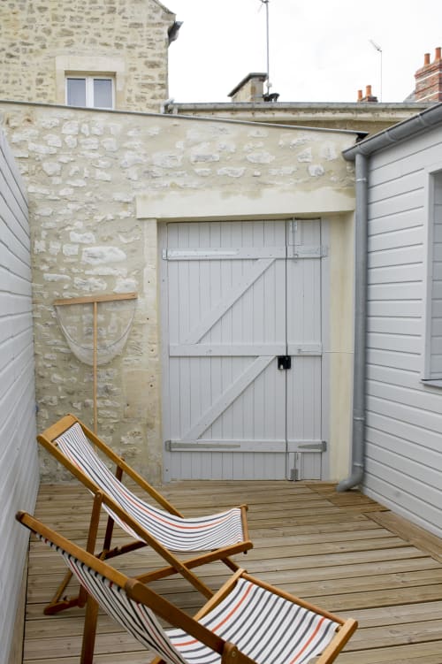 Coastal terrace at Les Filles du Bord de Mer with deck chairs, stone walls, and white wooden doors overlooking Port-en-Bessin