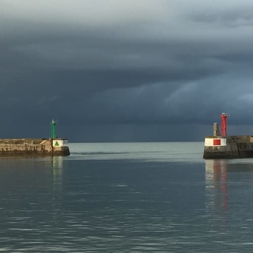 Nuages d'orage surplombant le port de Port-en-Bessin avec balises de navigation rouge et verte sur les jetées en pierre