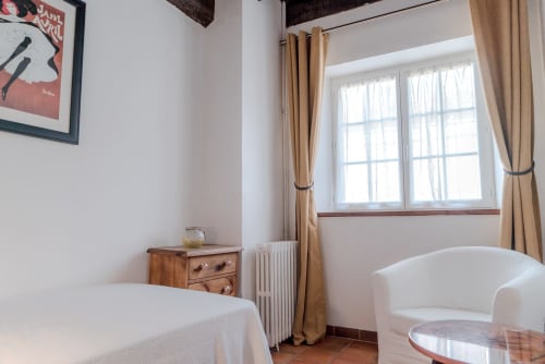 Chambre douillette au Pignié à Lescure-d'Albigeois avec lit blanc, table de nuit en bois et grande fenêtre aux rideaux beige