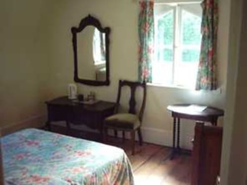 Chambre Tulipe du Chalet Du Bel Event B&B avec mobilier en bois foncé, miroir, bureau et vue sur le jardin à travers des rideaux fleuris