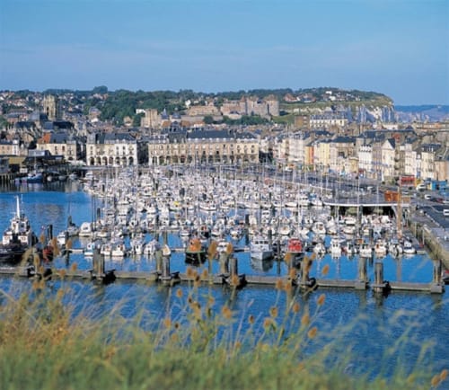 Scenic harbor view with hundreds of sailboats moored in blue water, European coastal town with stone buildings and hillside