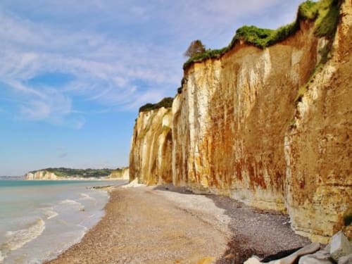 Dramatic chalk cliffs with green vegetation overlooking pebbly beach and turquoise sea near La Chapelle-sur-Dun