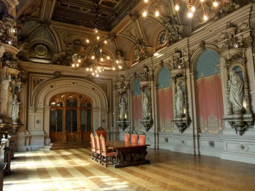 Ornate neoclassical ballroom with gilded ceiling, crystal chandelier, white columns, and red drapery at Chalet Du Bel Event