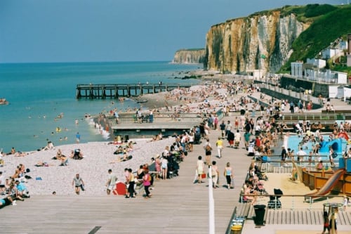 Crowded beach with pier, colorful umbrellas, and white chalk cliffs at La Chapelle-sur-Dun, France