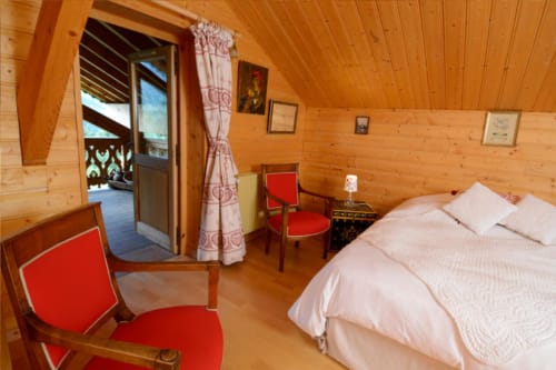 Chambre douillette à l'Auberge Nemoz avec poutres apparentes, chaises rouges, lit queen-size et accès à terrasse vue montagne au Haut-Bréda.