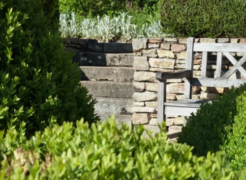 Stenen muur en houten poort van hotel Moulin Renaudiots in Autun, omgeven door verzorgde groene hagen en kruiden