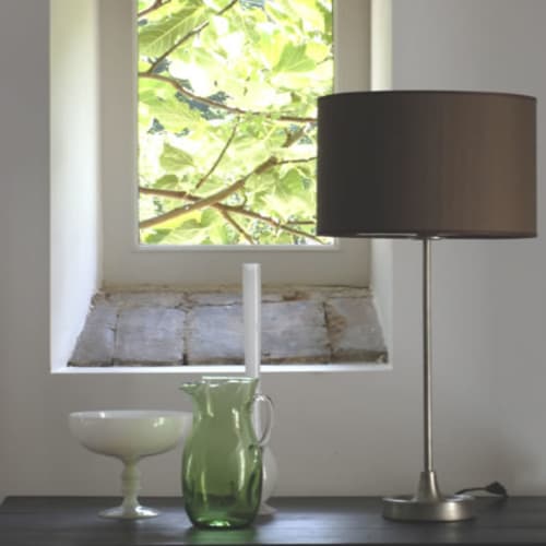Moderne lamp met zwarte kap naast groene glazen kan, uitzicht op de tuin van Hotel Moulin Renaudiots in Autun