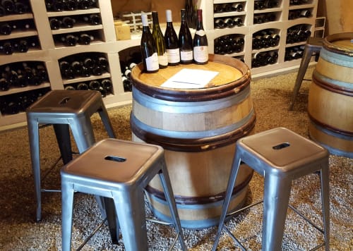 Wine tasting room at Moulin Renaudiots in Autun with barrel table, metal stools, and wine bottles on display shelves.