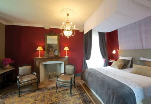 Chambre élégante du Château de Baylac aux murs cramoisis, lustre en cristal, cheminée et mobilier luxueux à Bugnein