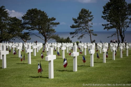 Croix blanches de cimetière militaire avec drapeaux français sur l'herbe verte, dominant la mer près de Port-en-Bessin-Huppain, France