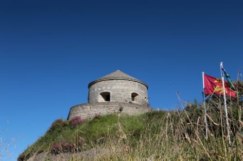 Tour de pierre historique sur la colline côtière de Port-en-Bessin avec drapeaux et végétation