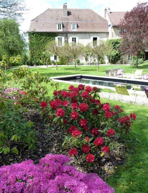 De tuin van Moulin Renaudiots met levendige rode en roze bloemen, zwembad en Franse landhuis in Autun