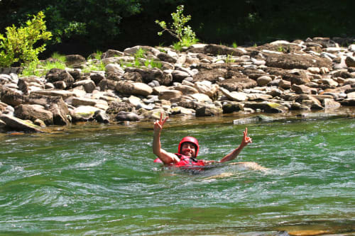 Personne nageant dans la rivière avec un casque rouge près du Château de Baylac, berges rocheuses bordées d'arbres verts