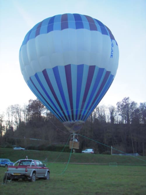 Mongolfière bleu et blanc amarrée au Château de Baylac à Bugnein, France avec véhicules de support