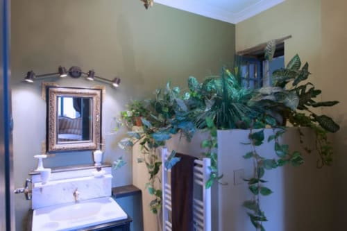 Salle de bains moderne à la Suite Lapis Lazuli du Château de Baylac avec plantes luxuriantes, miroir encadré et meuble-lavabo blanc