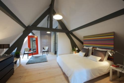 Suite Vivaldi au Château de Baylac à Bugnein : chambre loft contemporaine avec poutres apparentes, literie blanche et touches colorées