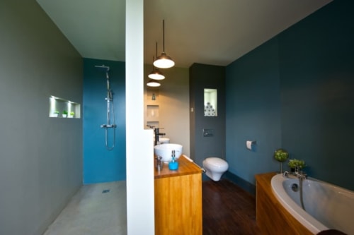 Salle de bain moderne du Château de Baylac avec mur d'accent bleu, meuble-lavabo en bois, baignoire îlot et luminaires suspendus