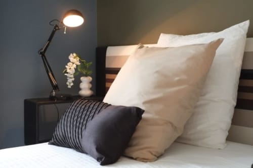 Chambre cosy du Château de Baylac avec oreillers blancs, coussin noir, et lampe articulée au-dessus de la table de nuit