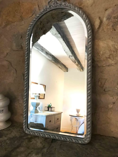 Ornate arched mirror reflecting bedroom interior with wooden furniture and exposed ceiling beams at Manoir De Rieuzal