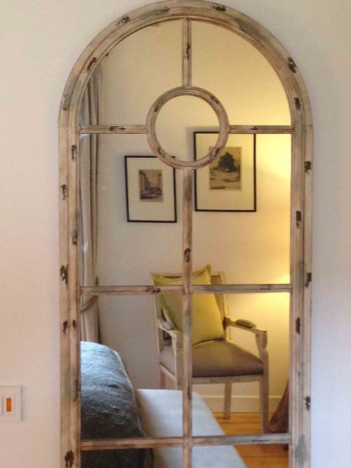 Arched doorway mirror at Manoir De Rieuzal in Loubressac reflecting bedroom with chair and framed artwork