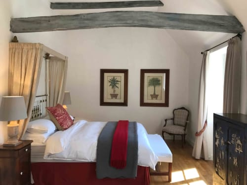 Elegant bedroom at Manoir De Rieuzal with exposed beams, queen bed, potted plant artwork, and mountain views in Loubressac
