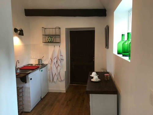 Compact kitchenette in Tilleul room at Manoir De Rieuzal, featuring white cabinets, red stovetop, and modern amenities in