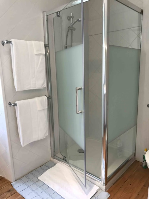 Modern glass shower enclosure with frosted panels, white towel racks, and tiled bathroom in Ciboulette room at Manoir De
