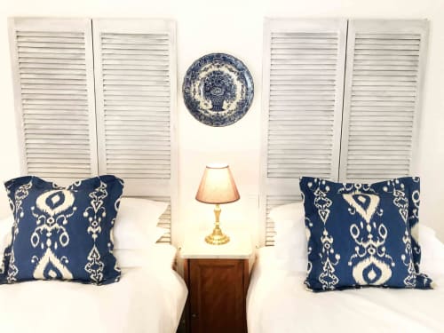 Twin bed setup at Manoir De Rieuzal with blue ikat pillows, shutters, and brass lamp in Loubressac