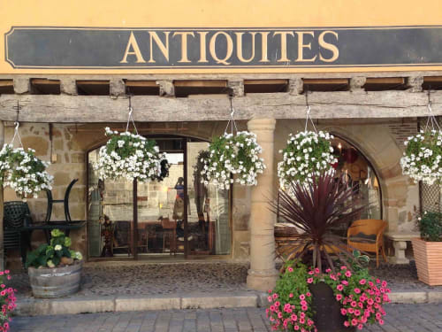 Charming antiques shop storefront at Manoir De Rieuzal in Loubressac with white hanging flowers and pink blooms