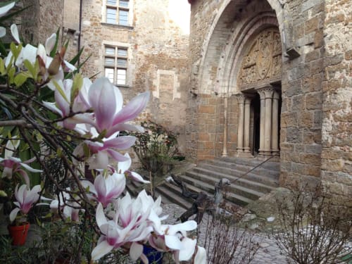 Pink magnolia flowers frame medieval stone entrance of Manoir De Rieuzal in Loubressac, France