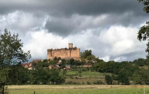 Medieval castle perched on hilltop overlooking lush countryside near Loubressac, France