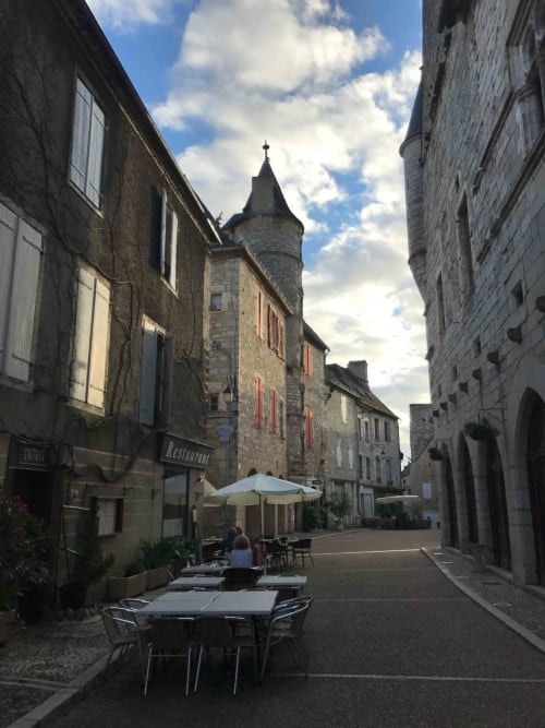 Medieval stone street with outdoor café seating, historic tower, Manoir De Rieuzal in Loubressac France