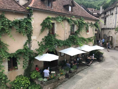 Ivy-covered stone building with white umbrellas at outdoor seating area in Loubressac, France