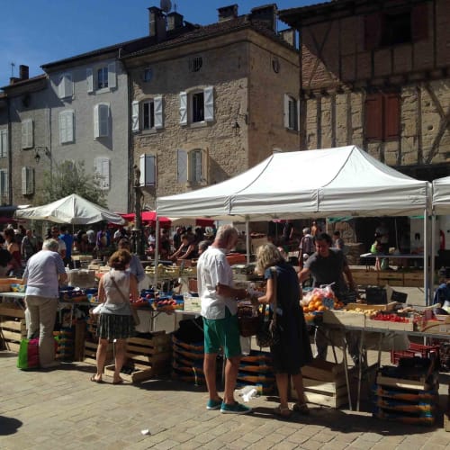 Outdoor farmers market in historic stone village square, Loubressac France with white tent canopies and produce vendors