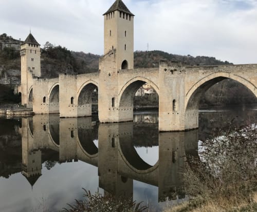 Medieval stone bridge with towers reflecting in calm water near Loubressac, France