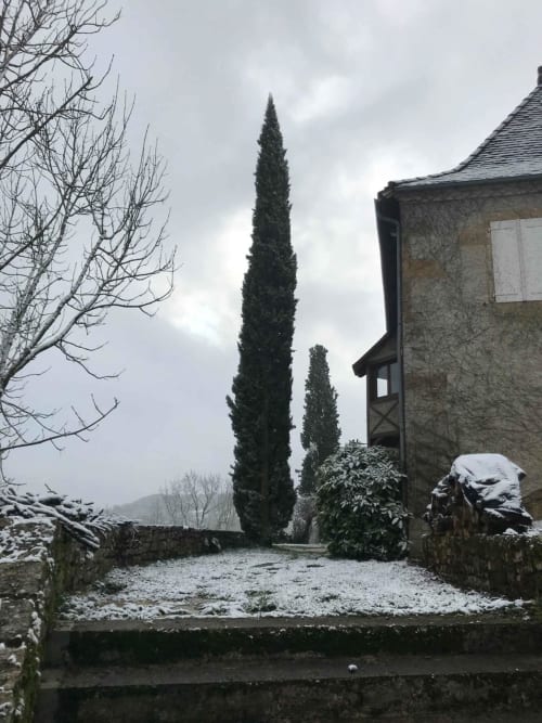 Snowy courtyard at Manoir De Rieuzal in Loubressac with cypress trees and stone building