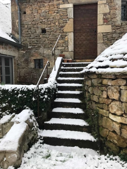 Snow-covered stone steps leading to dark wooden door at Manoir De Rieuzal in Loubressac, France