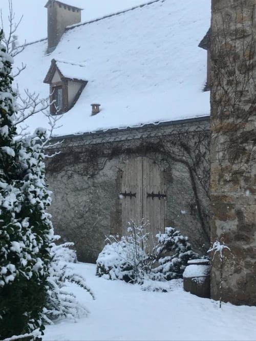 Snow-covered medieval castle entrance at Manoir De Rieuzal, Loubressac, with stone tower and wooden doors