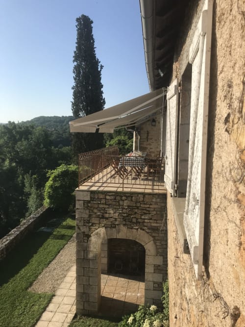 Stone terrace with awning at Manoir De Rieuzal in Loubressac, France overlooking landscaped grounds