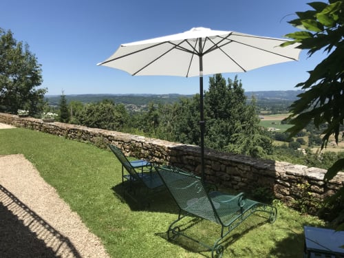 Cream umbrella over green loungers at Manoir De Rieuzal, overlooking Loubressac valley with stone wall and countryside views