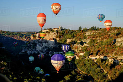 Hot air balloons floating above Loubressac castle and village in French countryside