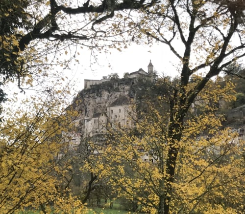 Medieval castle perched on rocky cliff framed by golden autumn trees near Loubressac