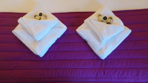 Deux sets de serviettes blanches avec amenités sur un lit violet à l'Hôtel La Trelade à St Martins