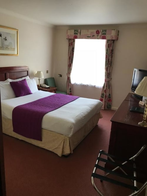 Chambre d'hôtel à La Trelade Hotel, St Martins avec lit queen-size, accents violets, fenêtre aux rideaux à motifs floraux