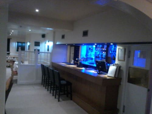 Bar moderne de l'hôtel La Trelade à Saint-Martin avec éclairage ambiant bleu, comptoir en bois, tabourets de bar et grandes baies vitrées