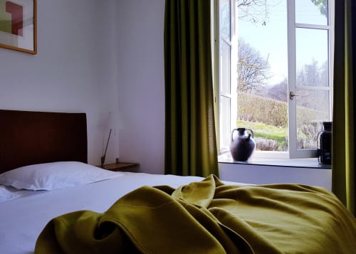 Slaapkamer Saint André in Moulin Renaudiots met uitzicht op het platteland door openstaande deuren, olijfgroene gordijnen en donkerhouten bed