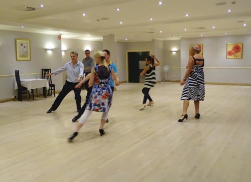 Cours de danse en cours dans le studio aux parquets en bois de l'Hôtel La Trelade à St Martin, les participants apprenant une chorégraphie.