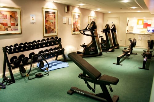 Centre de fitness moderne de l'Hôtel La Trelade avec haltères, vélos d'appartement, bancs d'exercice et sol vert à St