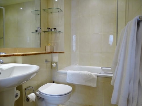 Modern bathroom in La Trelade Hotel Classic Twin Room with white pedestal sink, toilet, bathtub, shower enclosure, and