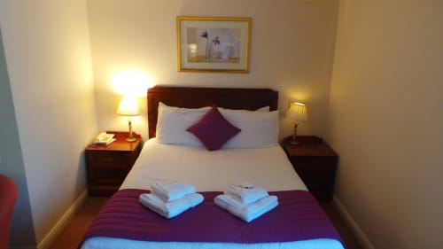 Chambre Double Classique à l'hôtel La Trelade avec éclairage chaleureux, lit en bois foncé, accents violets et serviettes blanches pliées